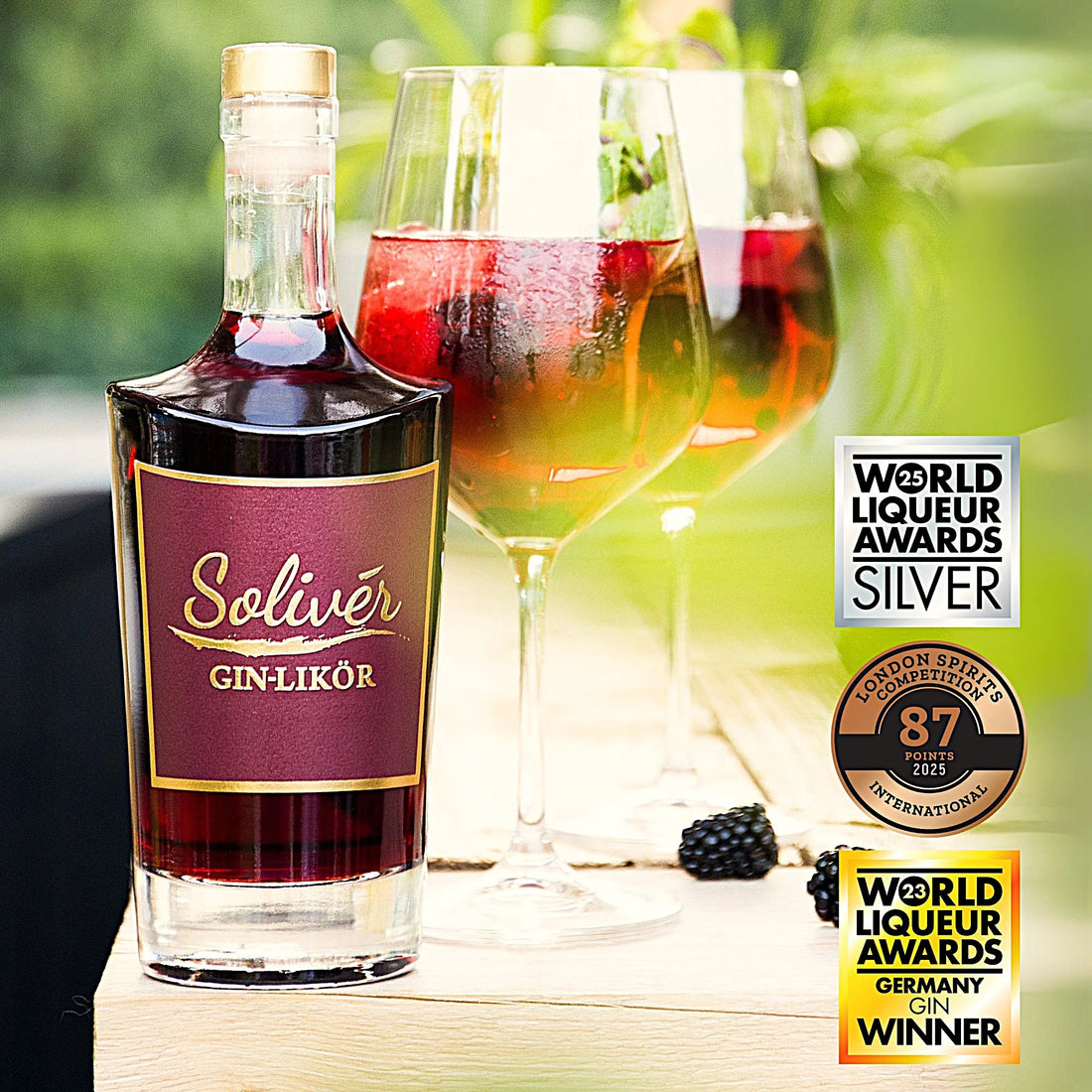 Solivér Brombeer Gin-Likör in eleganter Flasche, serviert auf Eis mit frischen Beeren in Weingläsern – sommerlicher Genuss im Freien“