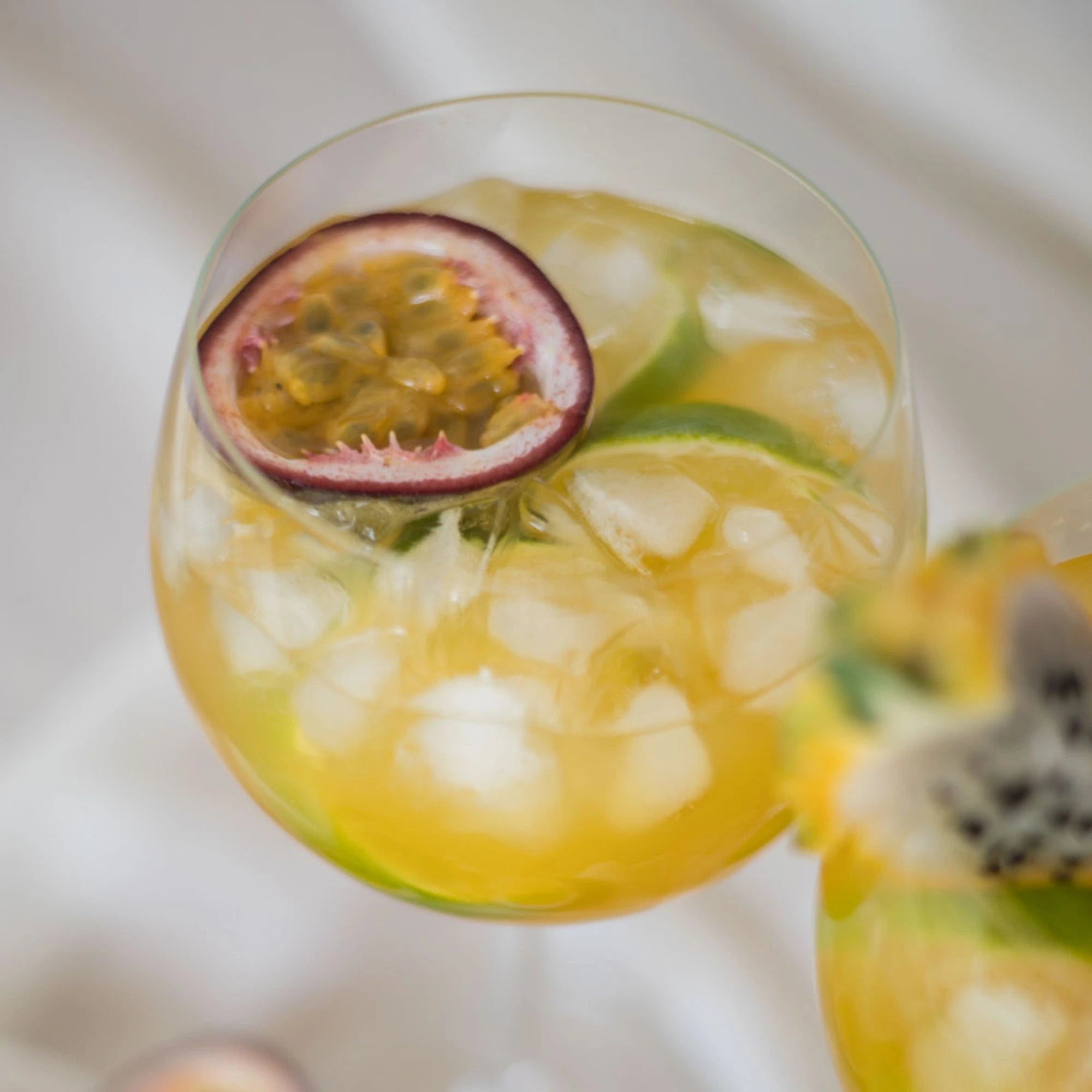 Erfrischender Cocktail mit Eis, Limette und halber Passionsfrucht in einem bauchigen Glas – tropischer Genussmoment.