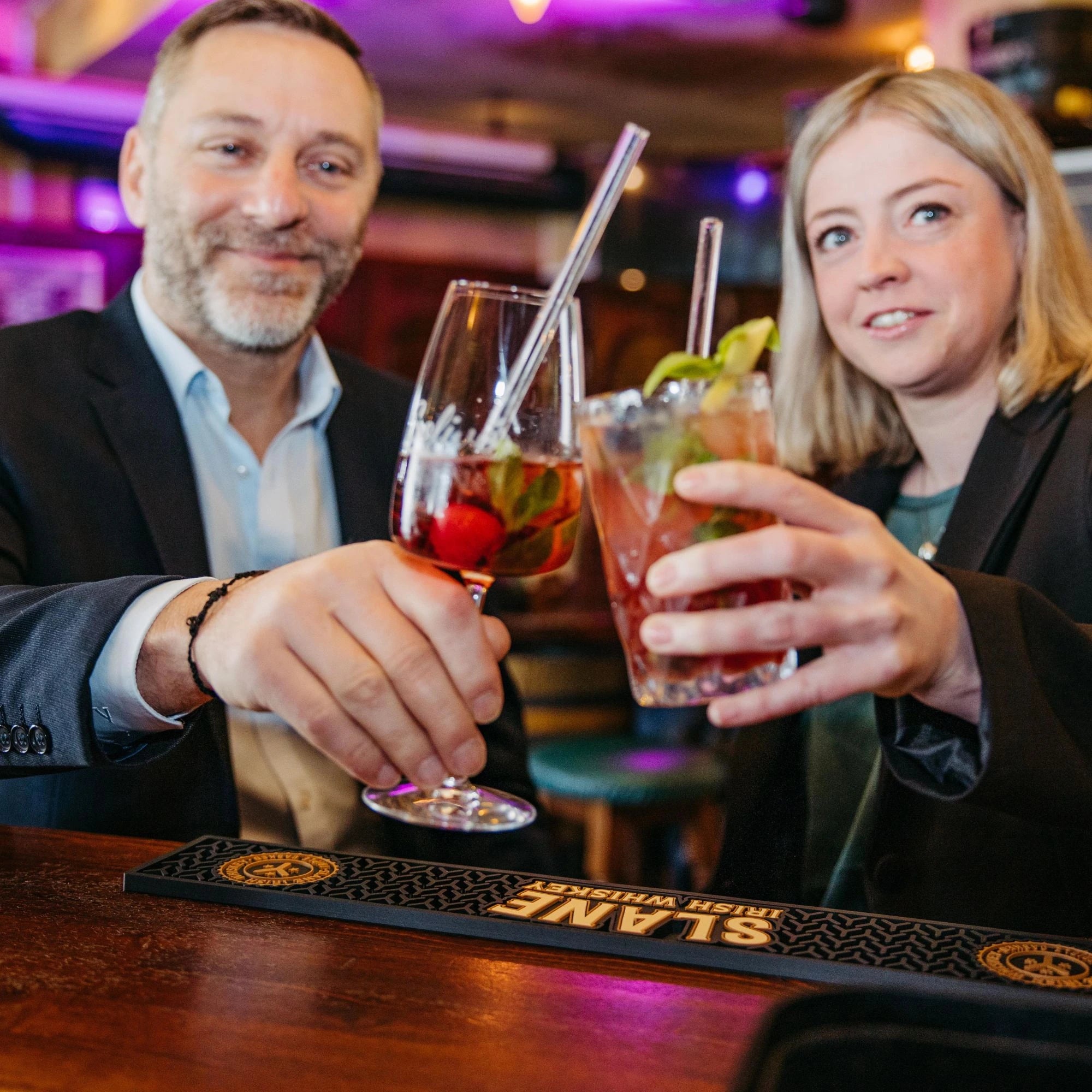 Ein Mann und eine Frau stoßen in einer Bar mit Aperitif und Cocktail Gläsern mit Solivér Brombeer Gin-Likör an.