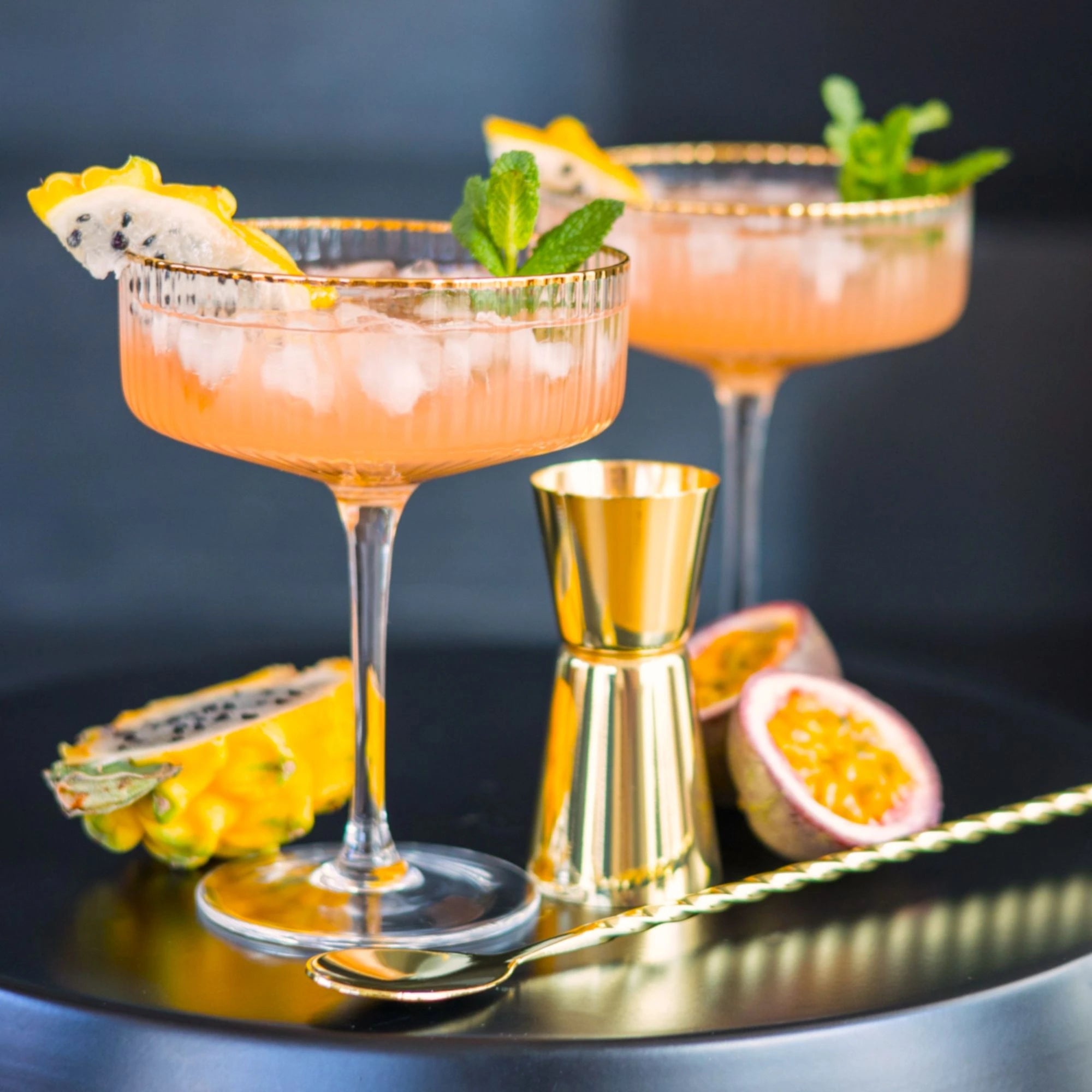 Zwei exotische Gin-Cocktails mit Eis, Minze und Drachenfrucht auf schwarzem Tablett.
