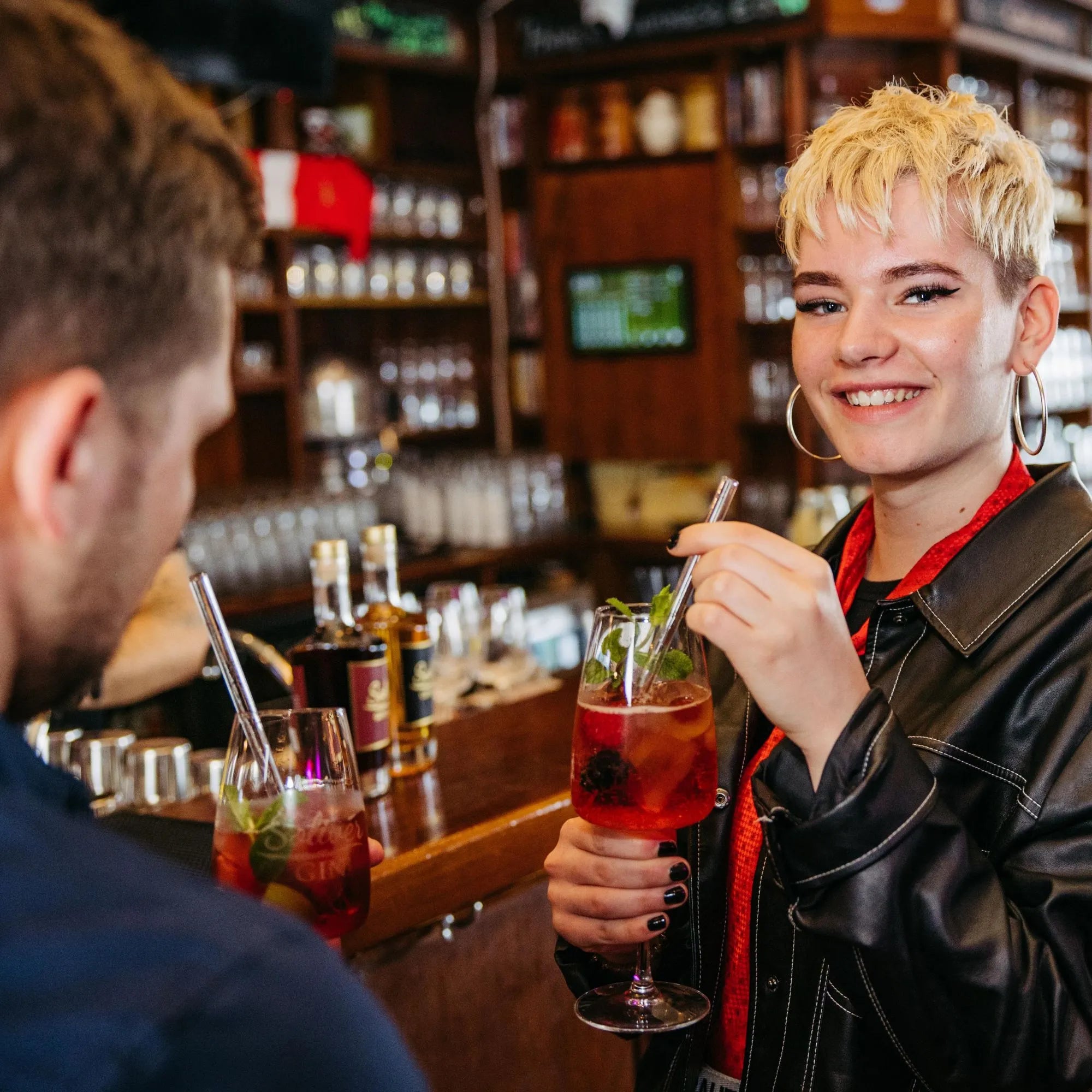 Junge Frau genießt Solivér Brombeer Gin-Likör Aperitif mit Eis und Beeren in geselliger Bar-Atmosphäre mit Freunden.