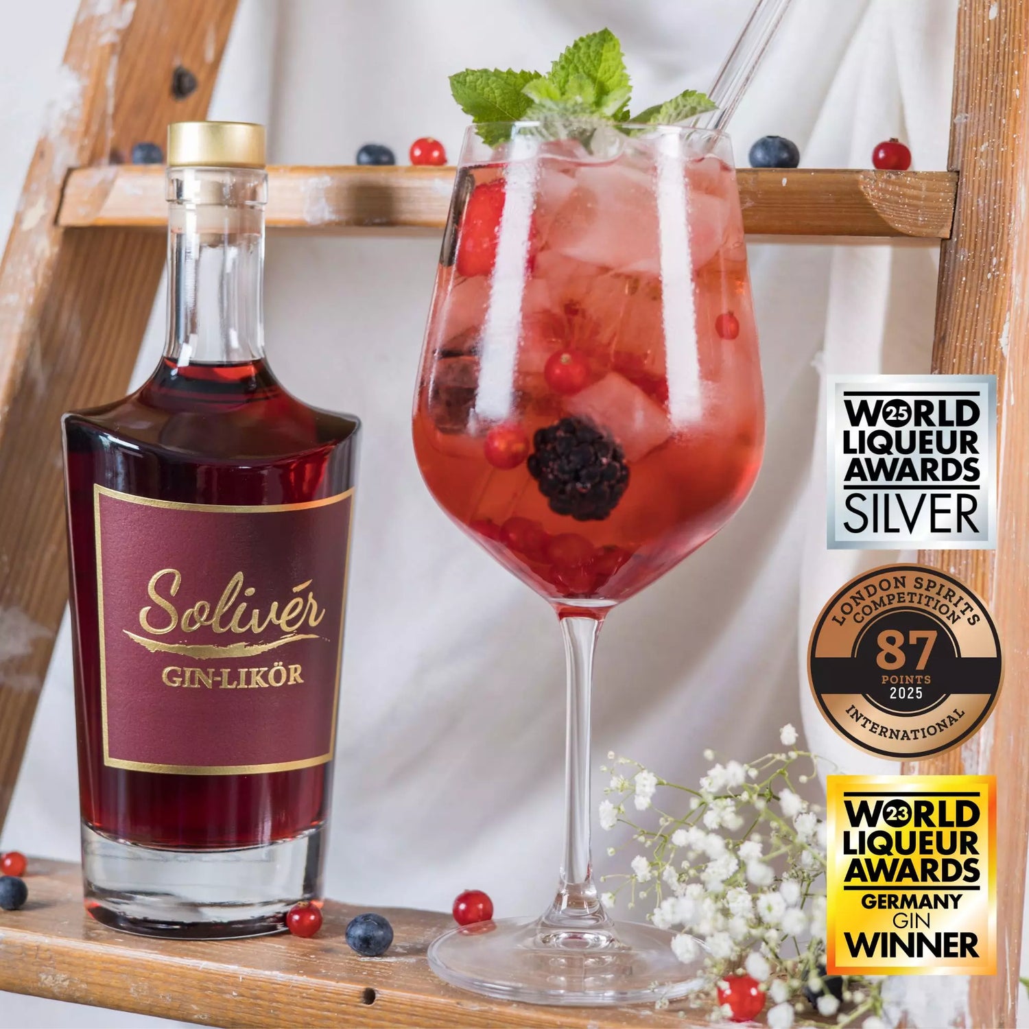 Solivér Brombeer Gin-Likör neben einem Cocktailglas mit Beeren, Minze und Eiswürfeln, ausgezeichnet mit internationalen Awards wie World Liqueur Awards und London Spirits Competition.