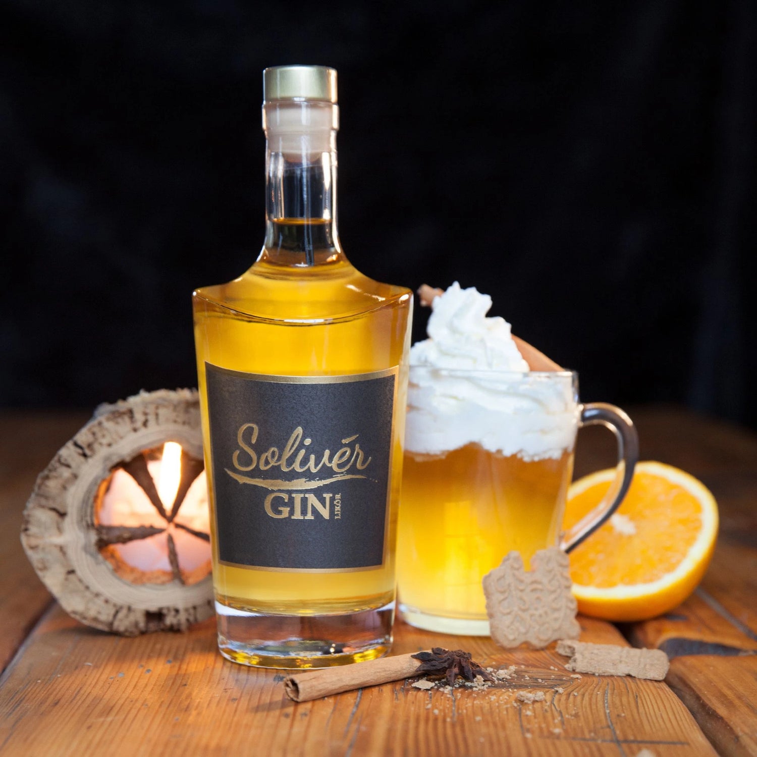 Solivér Gin-Likör mit Glüh-Gin im Glas, Sahnehaube, Gewürzen, Spekulatius und Orangenscheibe auf Holztisch vor dunklem Hintergrund.