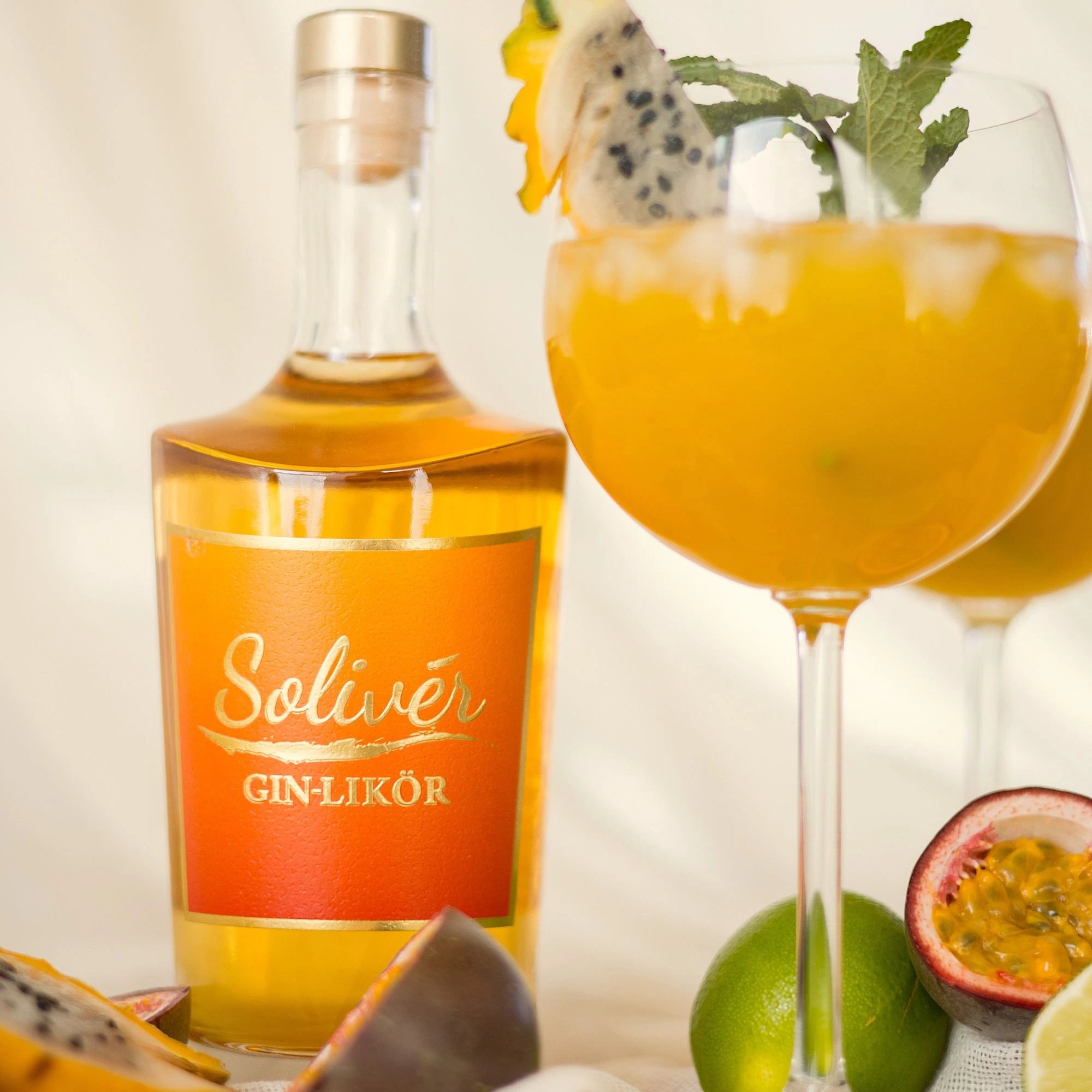 Solivér Gin-Likör in einer Flasche mit tropischem Aperitif im Glas, garniert mit Passionsfrucht, Drachenfrucht und Minze.