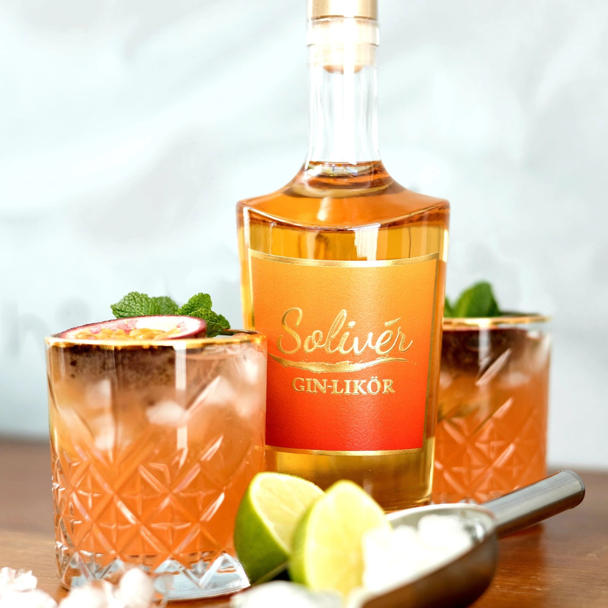 Solivér Mango-Maracuja Gin-Likör mit zwei dekorierten Cocktails, frischer Minze, Limette und Eiswürfeln – exotisch und erfrischend.
