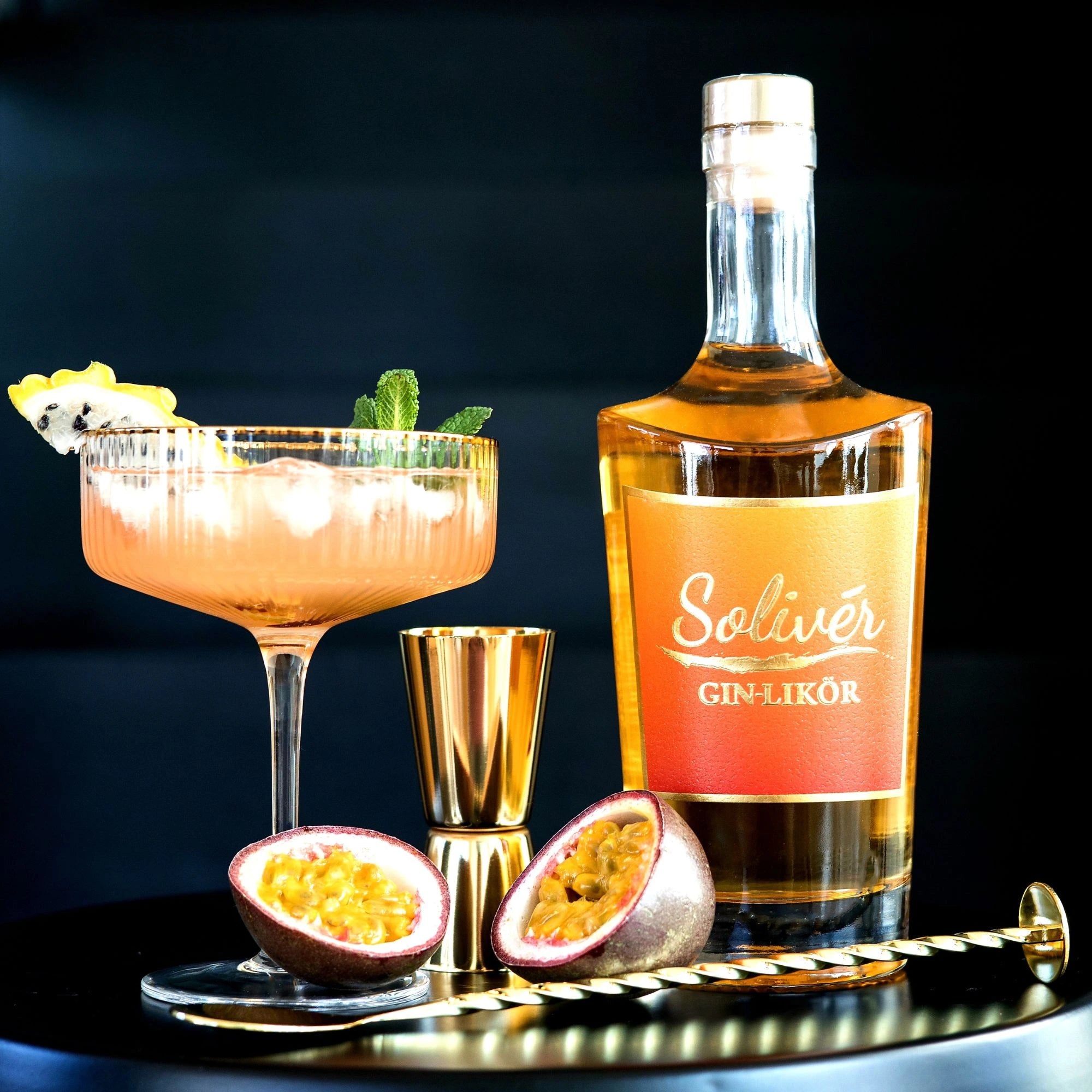 Solivér Mango-Maracuja Gin-Likör mit elegantem Cocktailglas, goldenen Baraccessoires und frischer Passionsfrucht – luxuriös inszeniert.