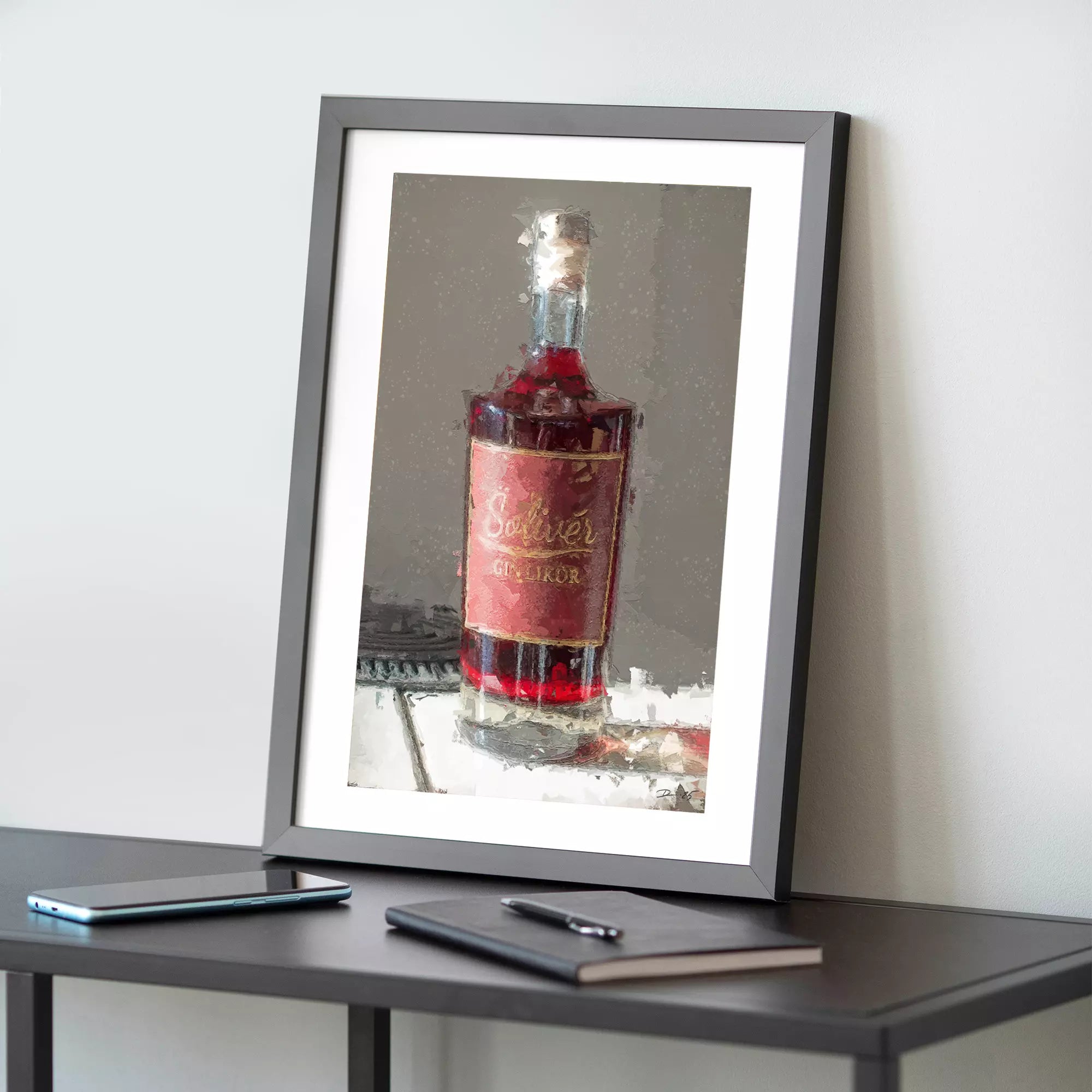 Gerahmtes Kustdruck mit künstlerischer Darstellung einer Solivér Ginlikör-Flasche mit rotem Etikett, auf einem Tisch neben Smartphone und Notizbuch.