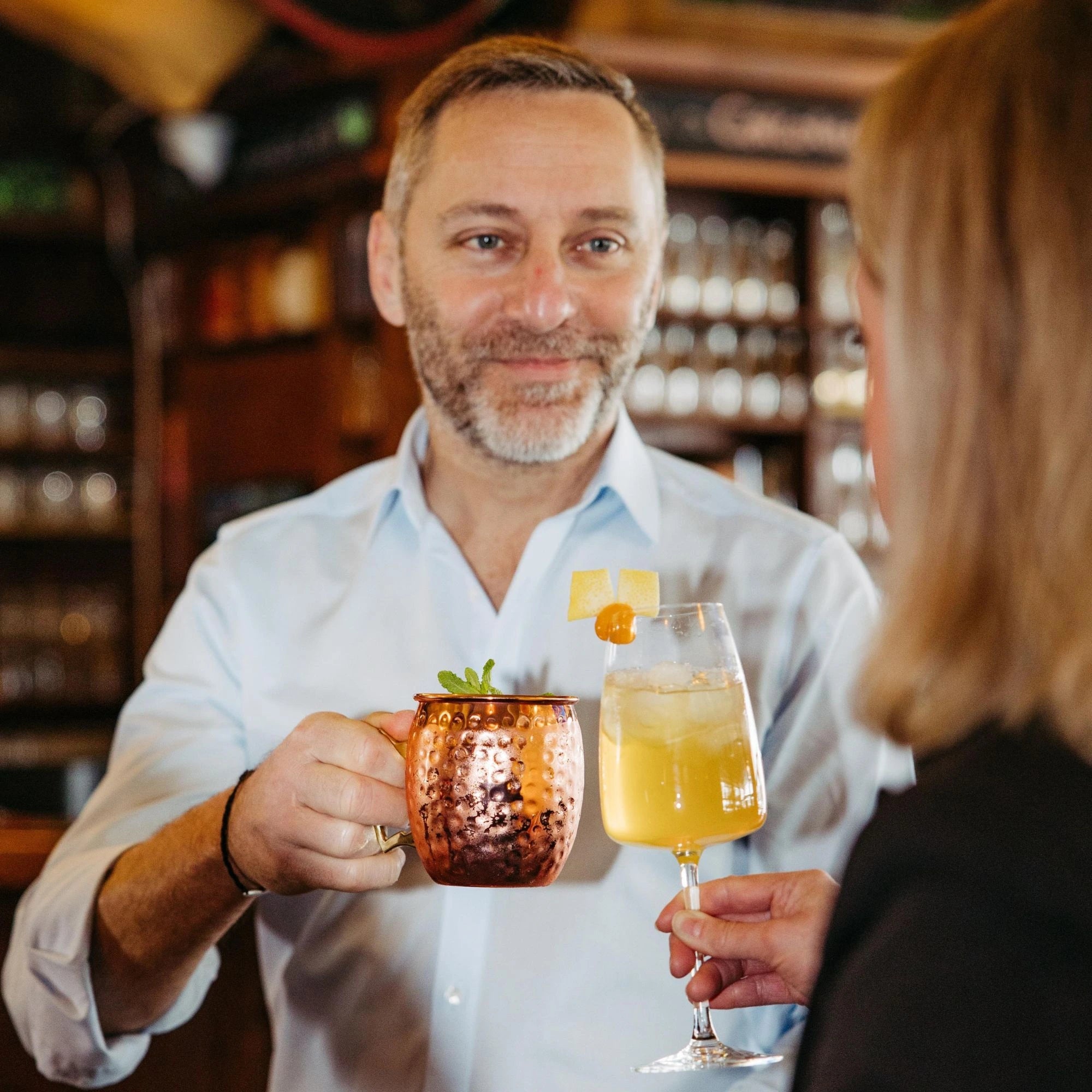 Ein Mann und eine Frau stoßen in einer Bar mit Cocktails auf Basis von Solivér Goldapfel Gin-Likör an.












