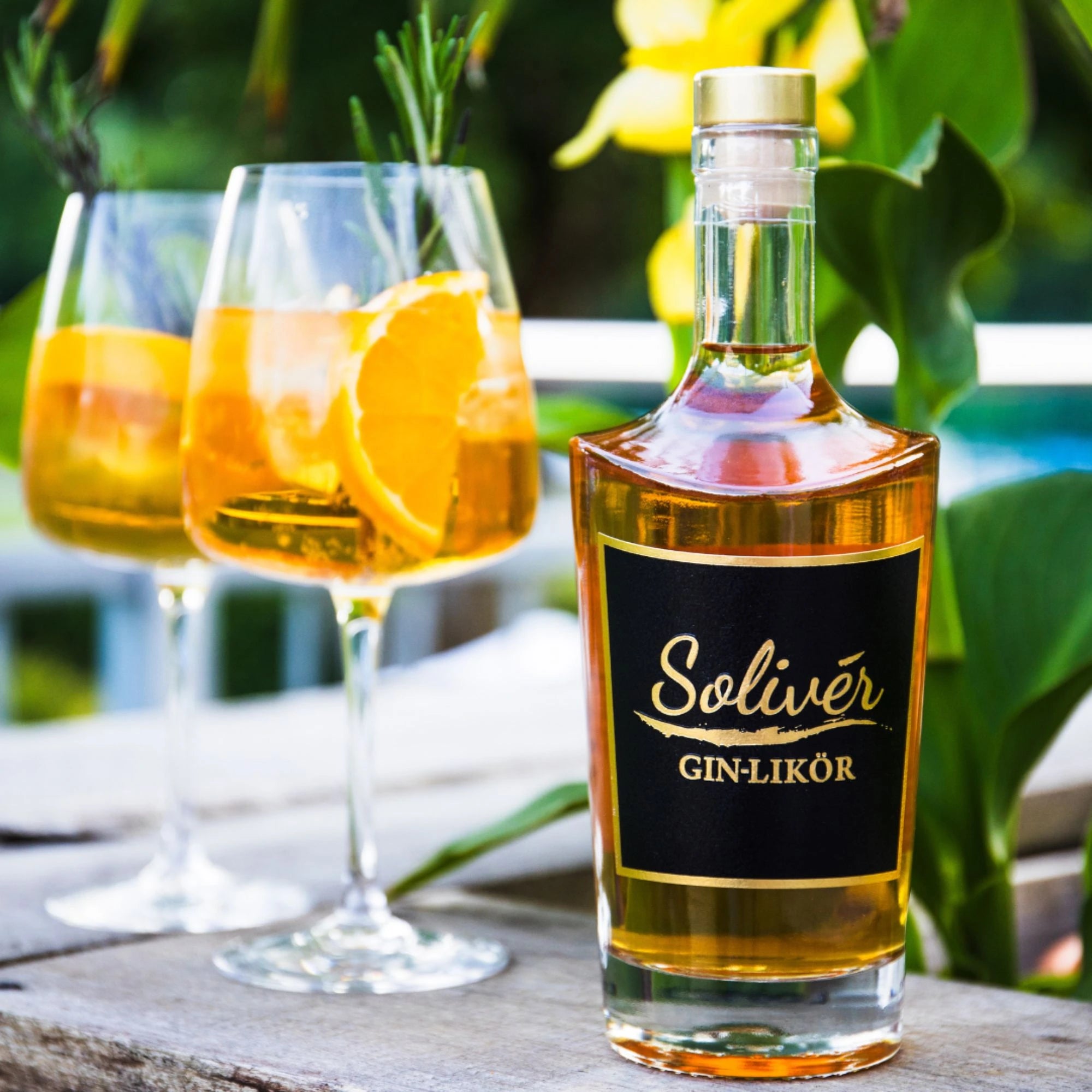 solivér ginlikör-flasche mit orangen-cocktail und rosmarin auf holztisch im garten